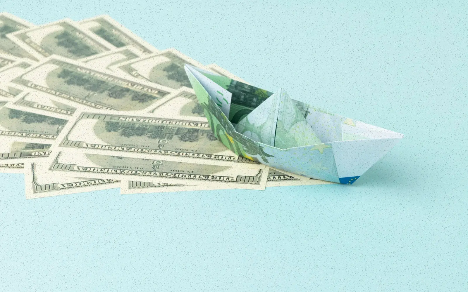 Cost to hire a SaaS product designer: paper boat folded from a euro note on a spread of hundred-dollar bills
